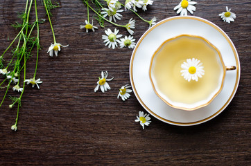 Obraz na płótnie Canvas herbal camomile tea in a porcelain cup on a dark wooden background