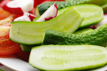 Segments of a fresh cucumber, tomato and garden radish on a plate, closeup. Vegetables from a bed