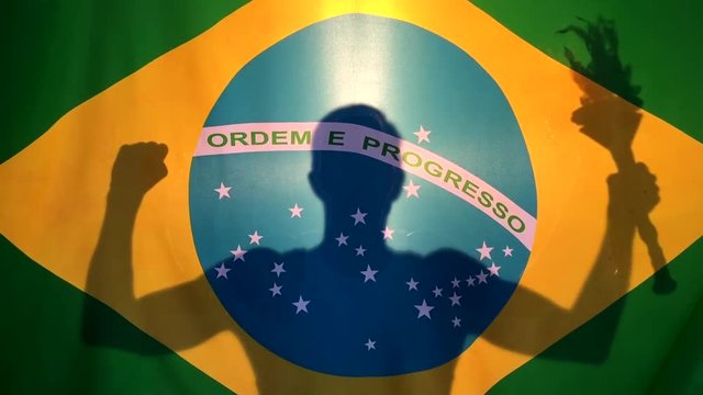 Brazilian athlete holding sport torch in silhouette behind Brazil flag background
