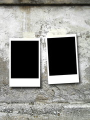 Close-up of two blank black rectangular instant photo frames with adhesive tape on gray weathered concrete wall background