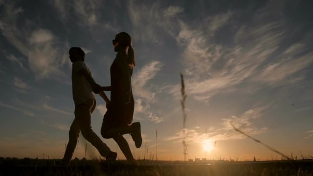 Silhouettes of happy couple running down at sunset