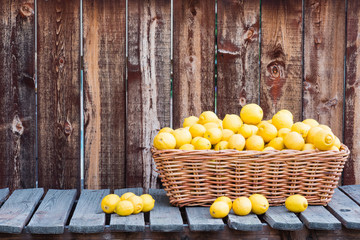 A basket of many lemons on a rustic plank table and background.
