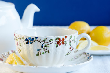 A teapot and a delicate china cup and saucer with lemon wedges on the side.