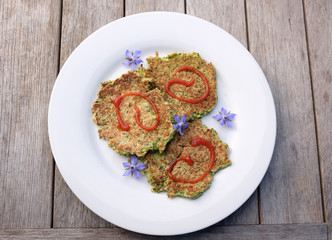 An easy lunch at home of zucchini or courgette fritters with tomato ketchup sauce and edible blue borage flowers on a timber outdoor table. Photographed in New Zealand.