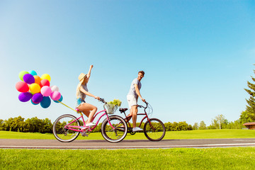 Two lovers riding bicycles with balloons on the background of sk © deagreez