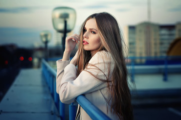 Beautiful lonely young pretty girl standing on the city roof in the sunset. Sensual evening portrait.