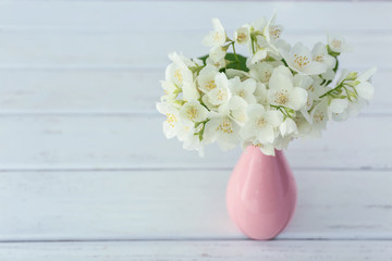 Fresh jasmine flowers in a vase on wooden background