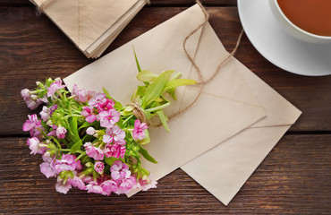 Bouquet of meadow flower with tea and envelopes on wooden table