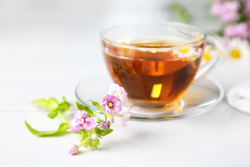 Beautiful meadow flowers and cup of tea on light background
