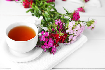 Obraz na płótnie Canvas Meadow flowers and cup of tea on light background