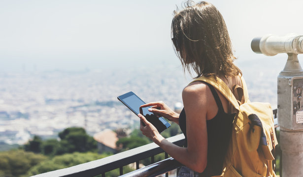Hipster young girl with backpack planning travel plan. Tourist traveler on background panoramic view of the city, binoculars. Mock up for text message. Barcelona. Female hands using tablet