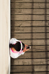 Top view of urban sporty woman taking a workout rest for texting on smartphone. Girl resting for listening music after fitness outdoor exercising.