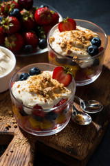 Assorted fresh fruit with custard in glasses on dark background