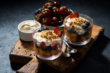 Assorted fresh fruit with custard in glasses on dark background
