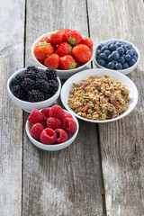 muesli and garden berries on wooden background, vertical