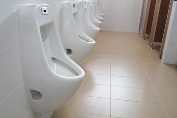 Modern white  urinals in public toilet room.