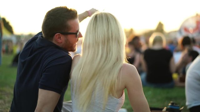 4k footage, couple sitting on festival meadow during summer sunset enjoying open air concert
