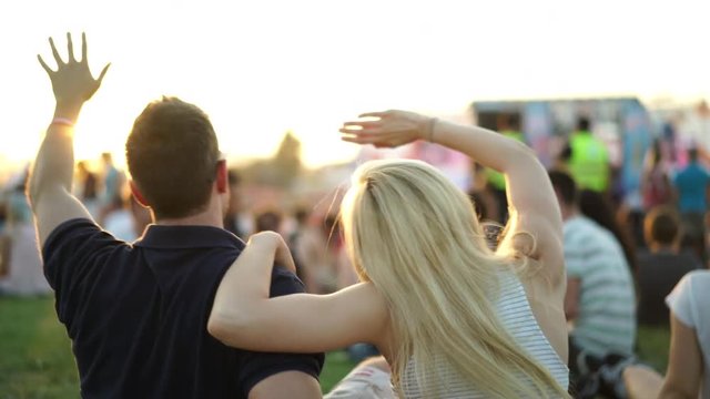 4k footage, back view young couple enjoying summer music festival at sunset, crowd and stage blurred
