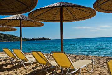 Straw parasols on a beach with ruins of old roman fortress in background, Sithonia, Greece