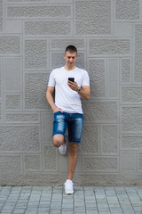 Young casual man using a smart phone texting messages in the str