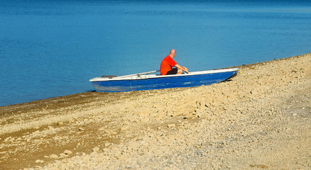 Small old fishing boat on a lake shore and man.