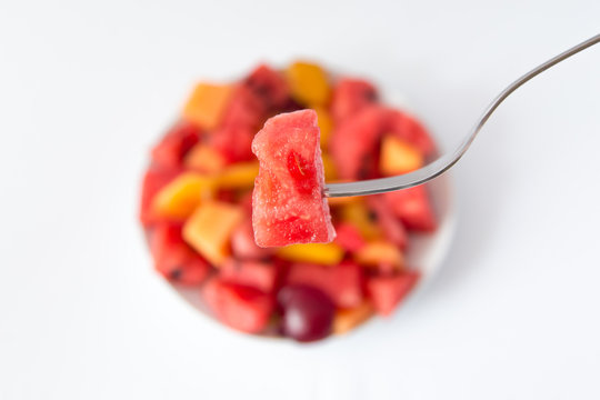 Boccone di cocomero su forchetta e su sfondo piatto di frutti estivi 