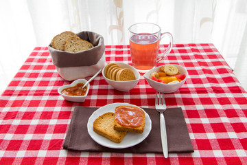 Fette biscottate con marmellata, te, frutta, biscotti e pane su tovaglia a quadri rossi e bianchi