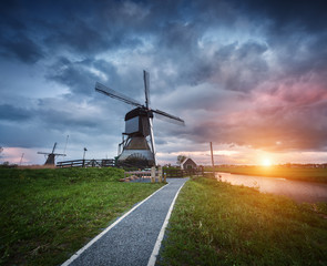 Landscape with traditional dutch windmills and path near the water canals. Clouds at colorful sunset in spring. Kinderdijk, Netherlands. Holland