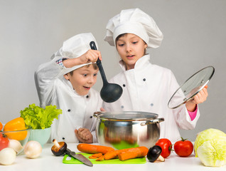 cooking little boy and girl looking in pan on table with vegetables