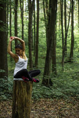 Beautiful sporty girl in the woods on a stump in yoga, sports