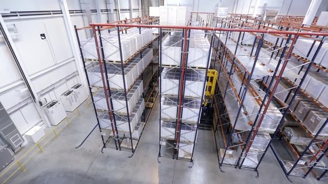Panorama of storage warehouse interior with lots of boxes, cardboards on shelves and moving yellow forklift.  