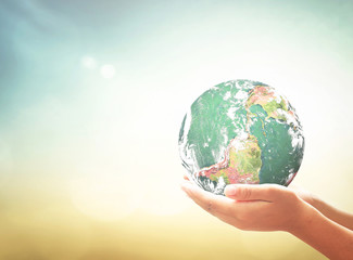 Earth Day concept: Earth globe in human hands over blurred nature background. Elements of this image furnished by NASA