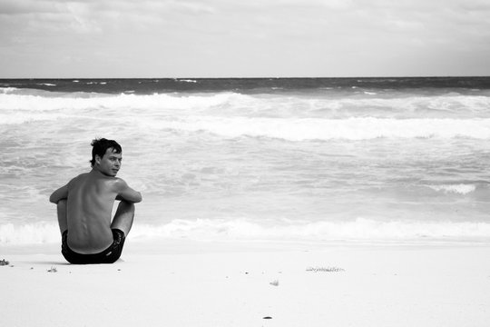 a young man sitting on the beach and thinks