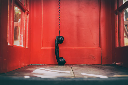 black handset hanging in a red telephone box. telephone receiver hanging touching the floor in a red call telephone booth. the concept of technological progress and the development of communication