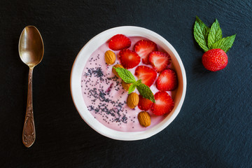 Breakfast bowl with yogurt,  granola or muesli or oat flakes, fresh strawberry and mint. Black stone background. Top view.