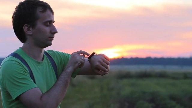 Man touching smart clock on the background of beautiful sunset sky