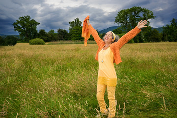 Happy mature woman standing countryside arms outstretched