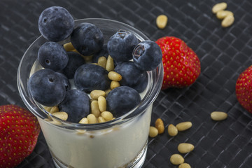 White bio yogurt with blueberries strawberries and pine nuts in glass on the black background