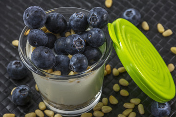 Green cap and glass of white yogurt with blueberries and pine nuts on the black background