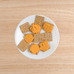Cheese on organic whole wheat crackers on a white plate atop a wood table.