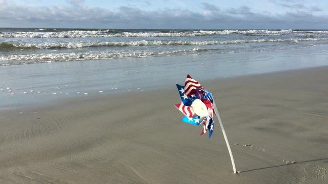 American flag design pinwheel twirling in the wind on a sandy beach