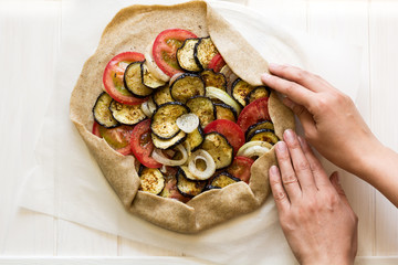 Homemade galette pie with grilled eggplants, tomatoes and onion on wooden background. Top view