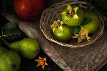 Green pomegranate in basket and fruits closeup background, dark photography.