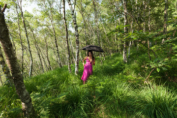 Woman walking in the woods with black umbrella