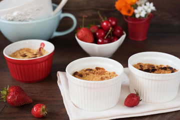 Cherry, strawberry crumble dessert in white bowls. Cherries, strawberries, flowers behind. Dark wood background