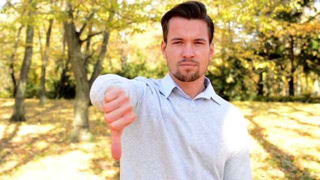 Young man stands in the woods and with serious face shows thumb down