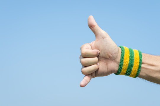 Athlete hand with yellow and green Brazil colors wristband giving a classic shaka surfer sign against blue sky