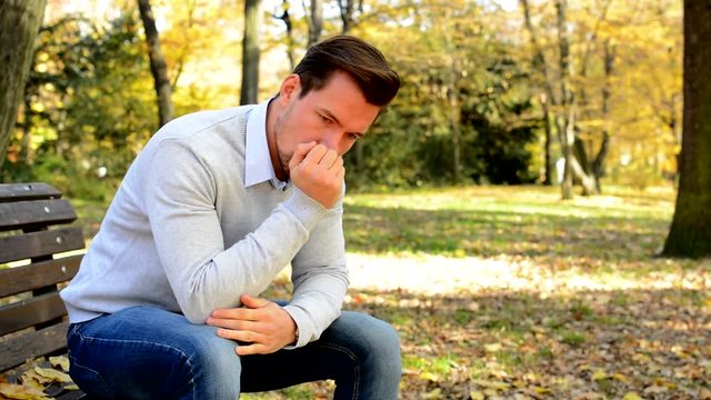 Young man sits on bench in a park, is nervous, sad and thinks