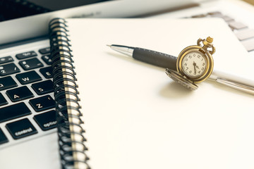Vintage watch on spiral open notebook and pen on top of laptop