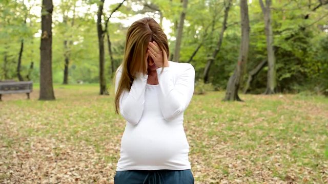 Young pretty pregnant woman crying in park